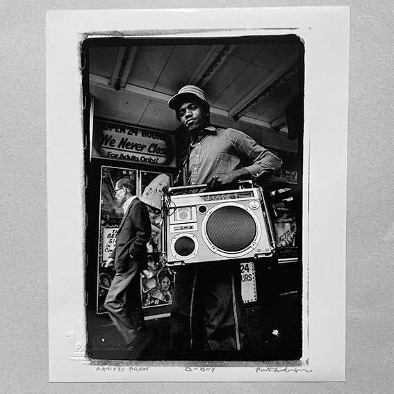 Black and white photograph of a man holding a boom box, with a store in the background, signed and stamped as an artist's proof.